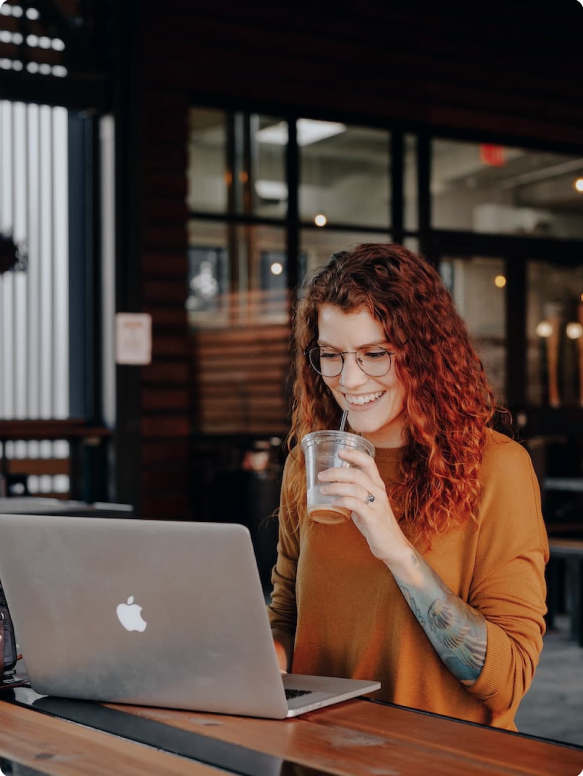 Woman standing in front of a laptop, drinking an iced coffee through a straw.